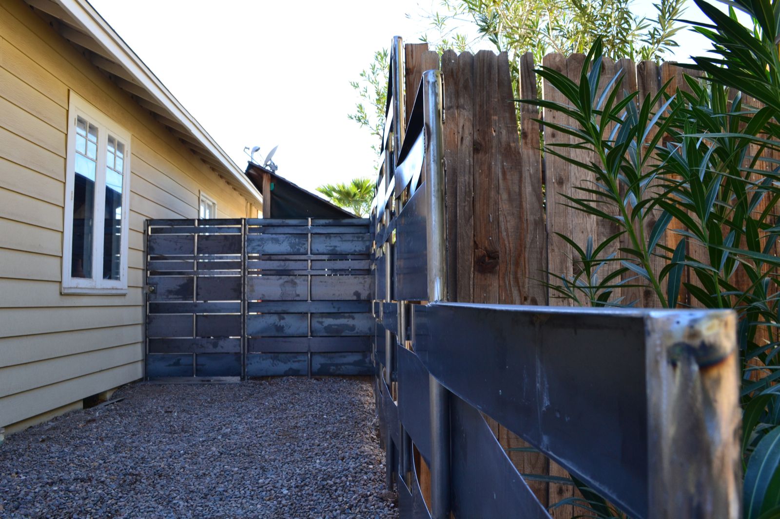 Weaved raw steel fence with gate. Built with various width steel sheets that are weaved in and out of round steel tube posts.