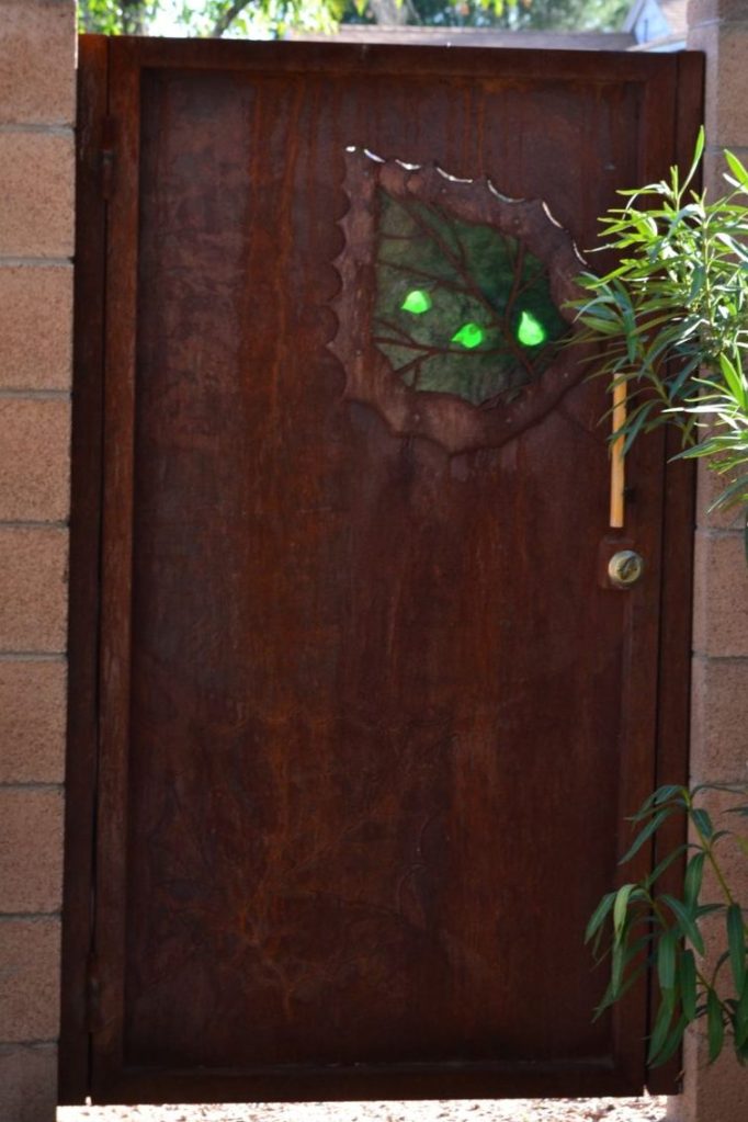 Rusted steel gate with wood handle, textured green glass insert in leaf shaped metal cut out.
