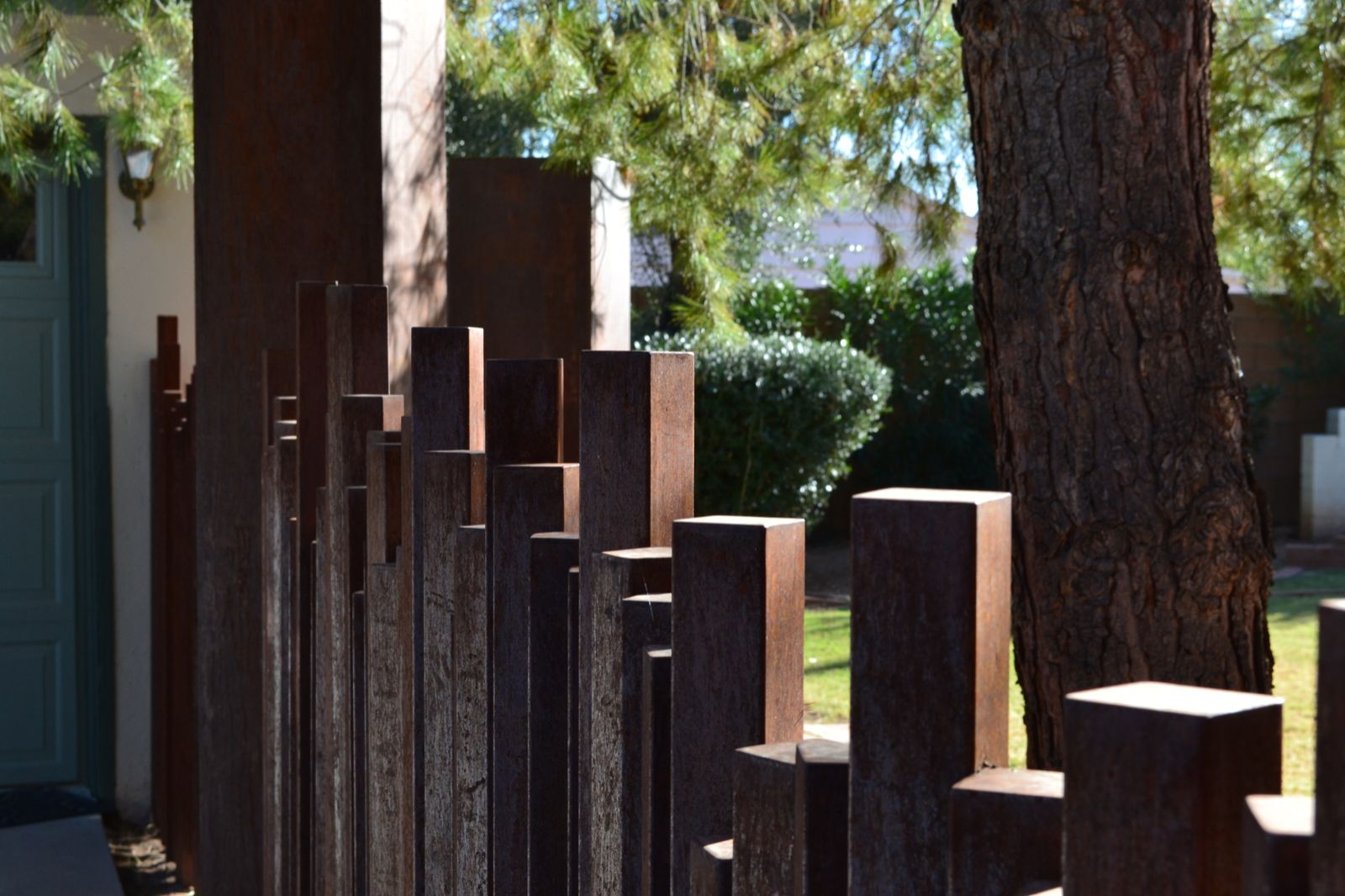 Detail photo of a raw, rusted steel fence and gate with rusted square tubes that are capped with steel plates that create the fence.