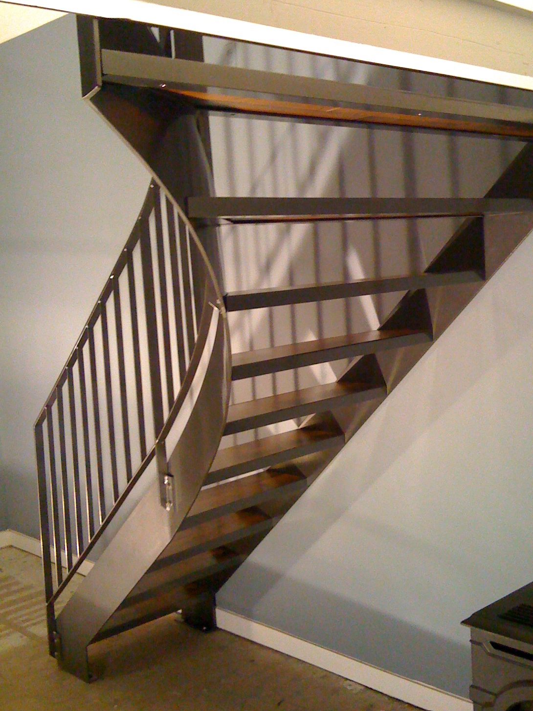 Curved steel stair with antrazite color tone, Wood step insets and railing, going from first to second floor in a cabin in Crown King AZ.