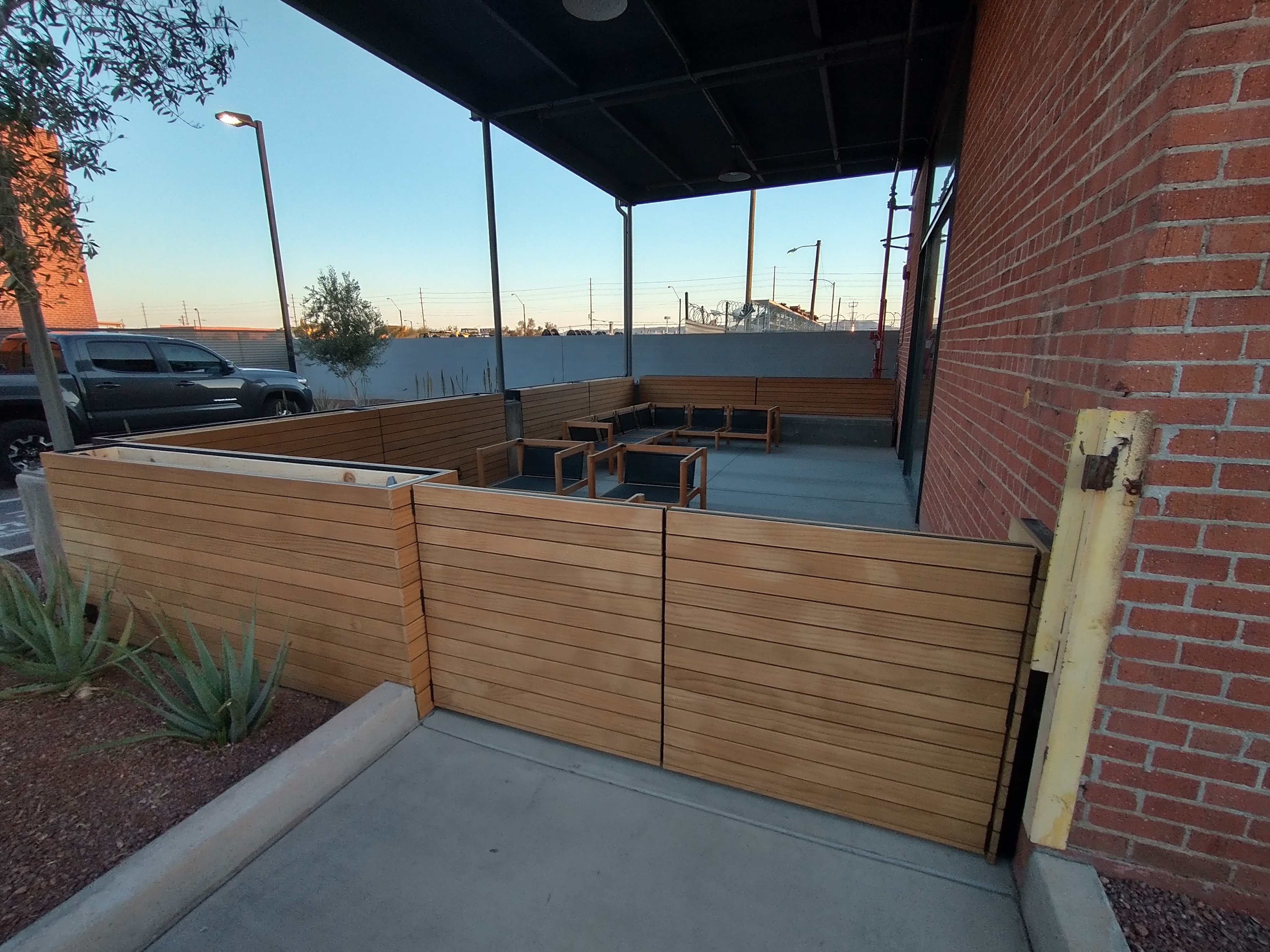 Coral building steel planter pots that create an outdoor showroom for outodoor furniture company. Steel planter boxes are sided with 3" wood slats that run horizontally. Wood has a teak wood look. Product name of wood is Lignia.