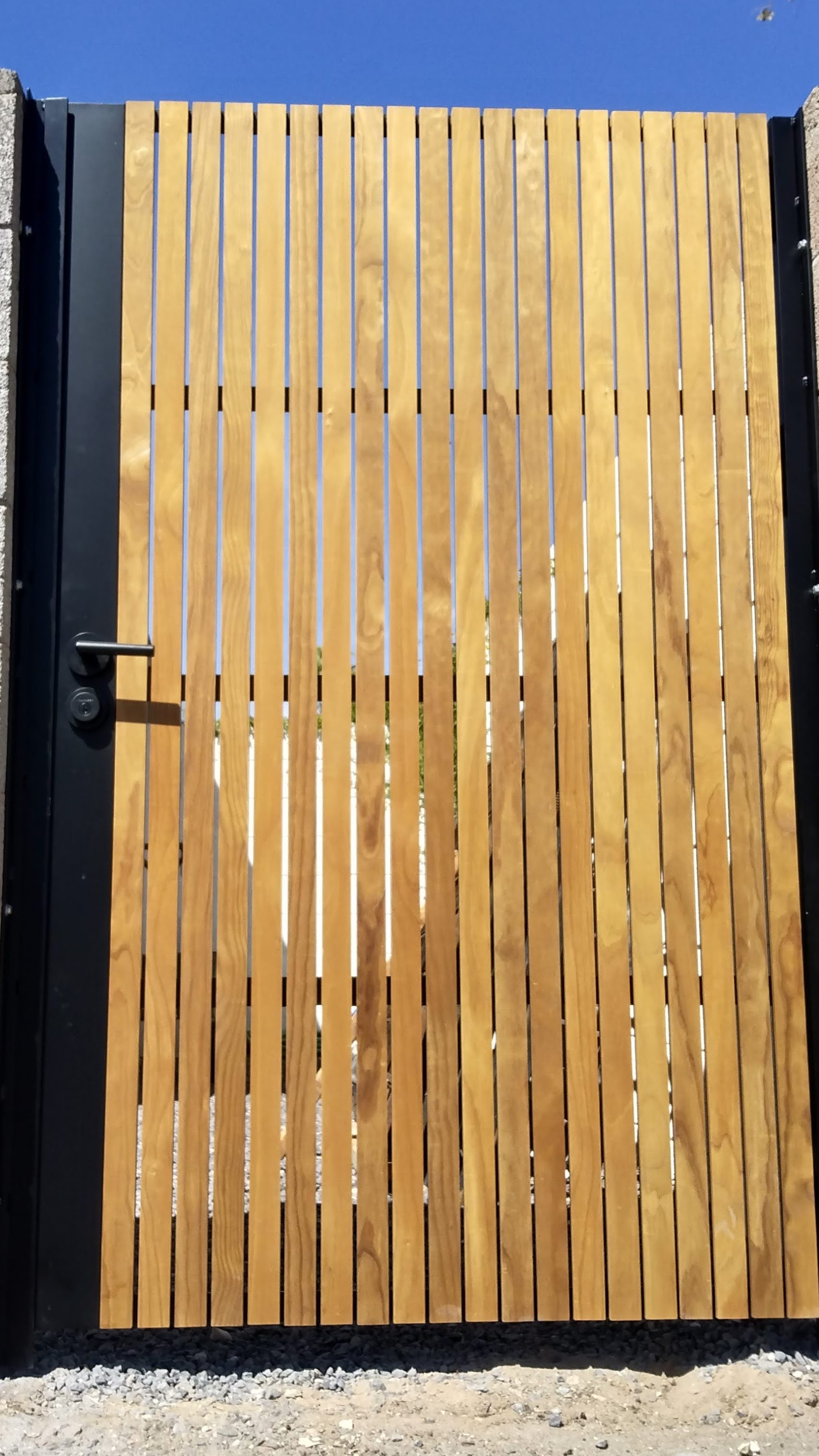 Alley steel gate, power coated black with 2" cedar, teak, Lignia fencing slats. Handle lock and deadbolt lock.